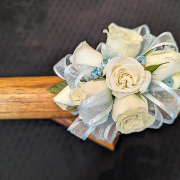 Small cluster of white roses with blue ribbon and blue gems arranged as a corsage