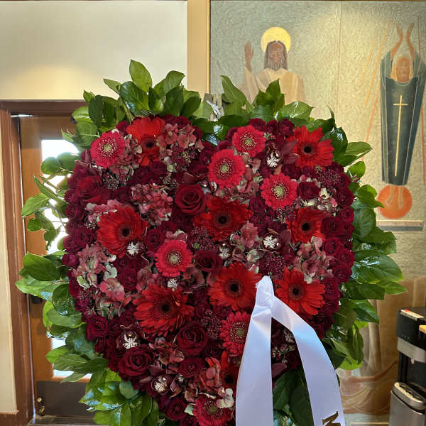 Heart-shaped red floral wreath on an easel with white ribbons