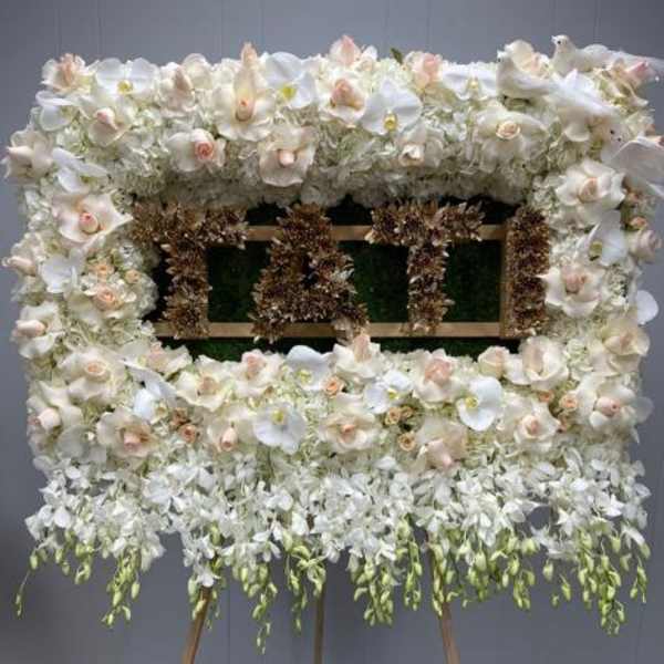 Large white floral standing arrangement on an easel with a central sign
