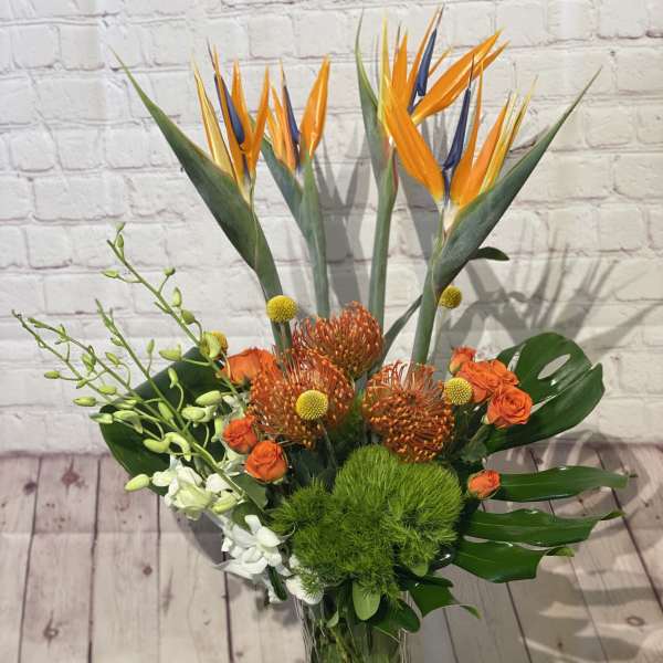 Tropical bouquet with bird of paradise, orange roses, and green filler in a glass vase