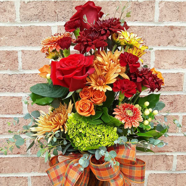 Autumn bouquet of red, orange, and yellow flowers in a glass vase with plaid ribbon