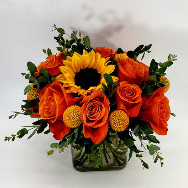 Orange roses and a yellow sunflower in a glass vase