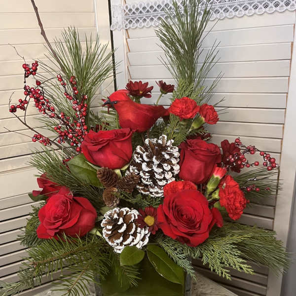 Red roses and carnations in a glass vase with pinecones and evergreen branches
