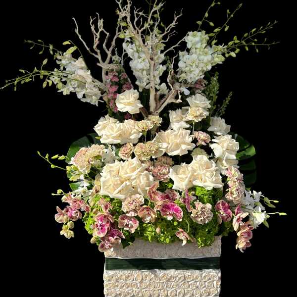 Tall floral arrangement with white orchids, cream roses, and pink blooms in a decorative box