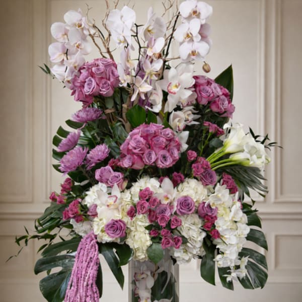 Tall floral arrangement with pink roses, white orchids, and hydrangeas in a glass vase