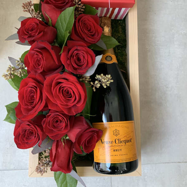 Red roses arranged with a champagne bottle and gift box in a wooden tray