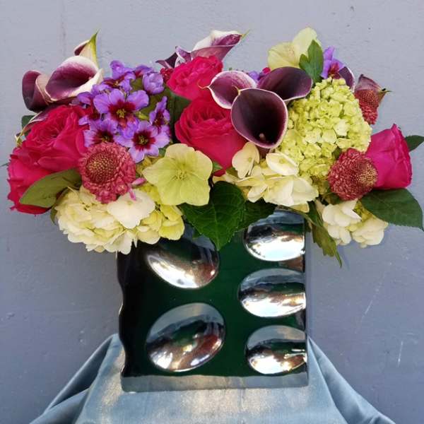 Mixed bouquet with pink roses, purple flowers, and calla lilies in a green vase
