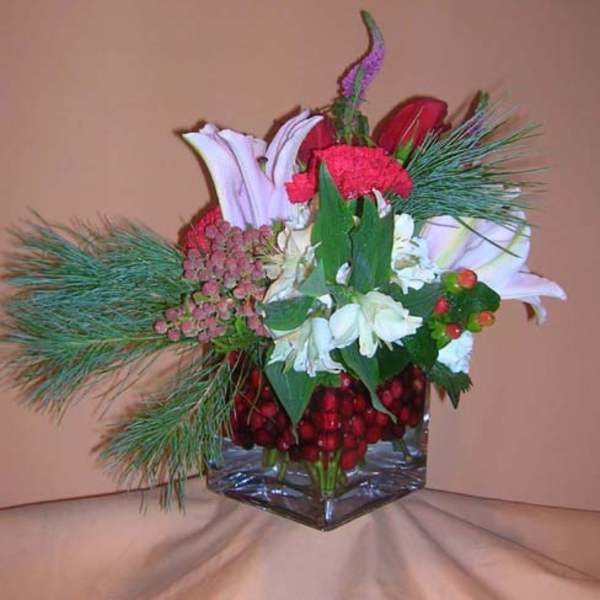 Mixed bouquet with lilies, carnations, and pine in a glass vase