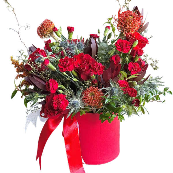 Red floral arrangement in a pink hatbox with ribbon