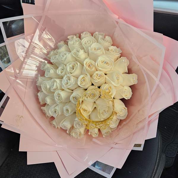 Bouquet of white roses wrapped in pink paper with a gold handle