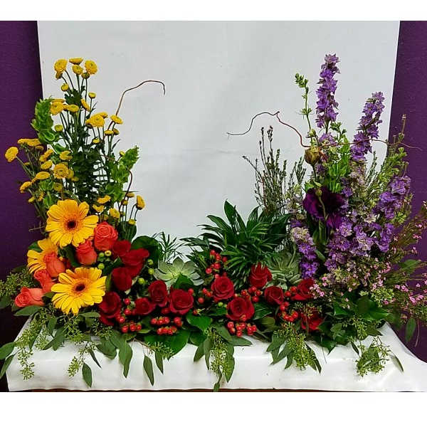 Large floral arrangement with red roses, yellow daisies, and purple spikes