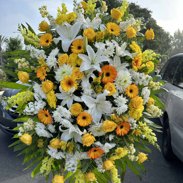 Large standing spray of white lilies, yellow roses, and orange gerbera daisies
