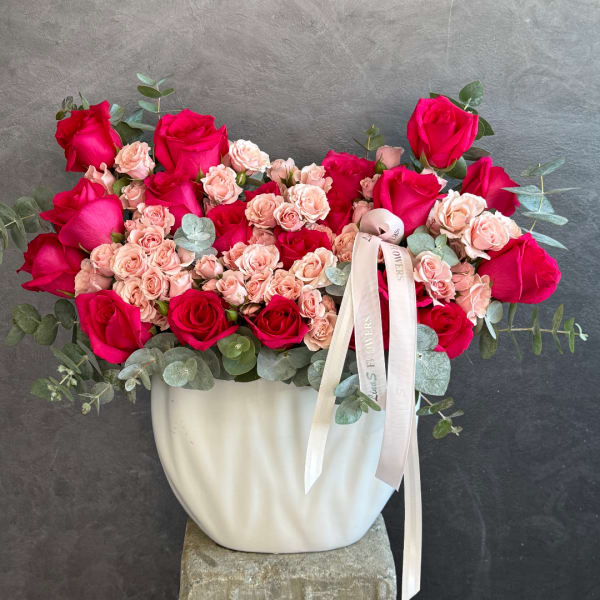 Pink and blush roses arranged in a white vase with ribbon