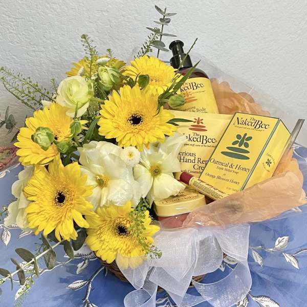 Yellow and white flowers arranged with bath and body gift items in a basket