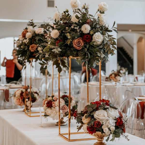 Tall floral centerpieces with roses and greenery on gold stands at a reception table