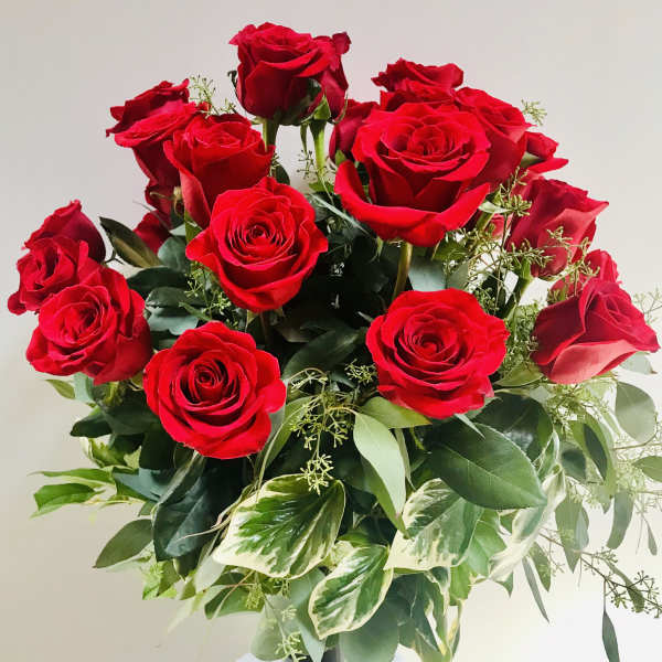 Arrangement of red roses with variegated foliage in a tall dark glass vase