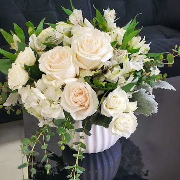 White and cream rose arrangement with greenery in a white textured pot on a black table