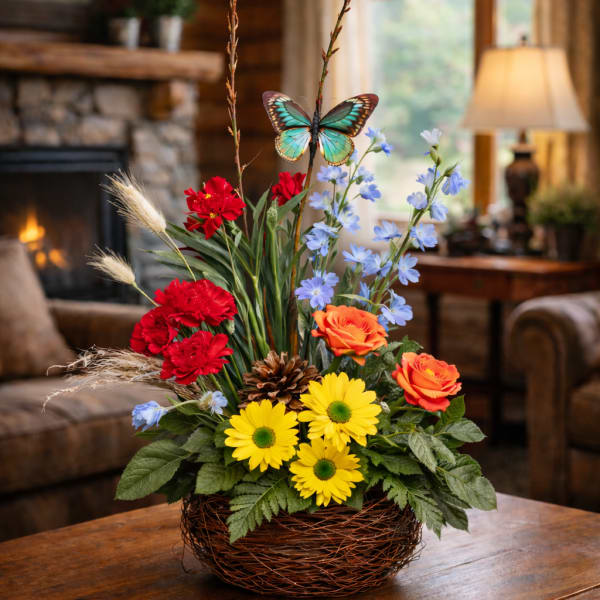 Basket arrangement with red, orange, yellow, and blue flowers and a butterfly pick