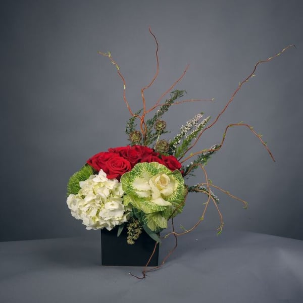 Red roses and white hydrangeas in a black square vase with curly branches