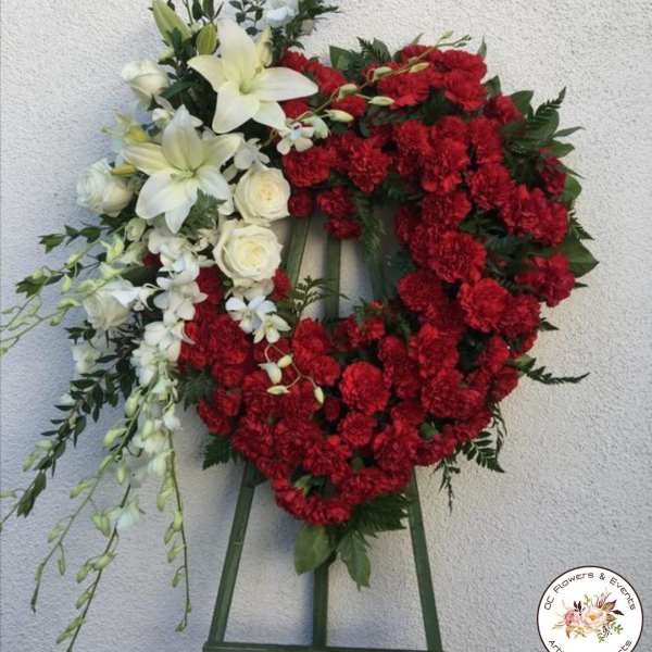 Heart-shaped floral wreath with red carnations and white lilies on an easel