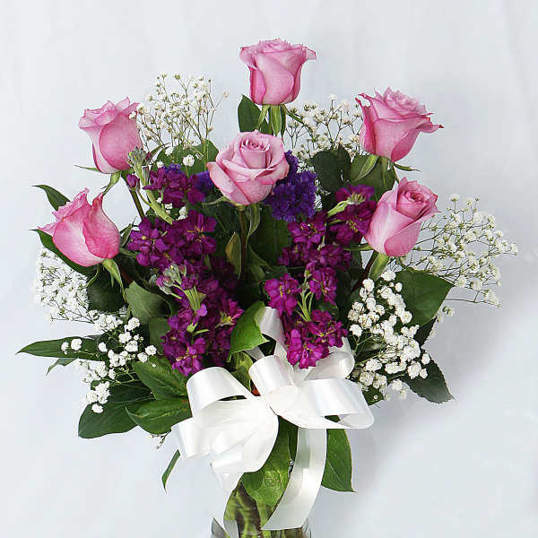 Pink roses and purple flowers in a glass vase with a white ribbon