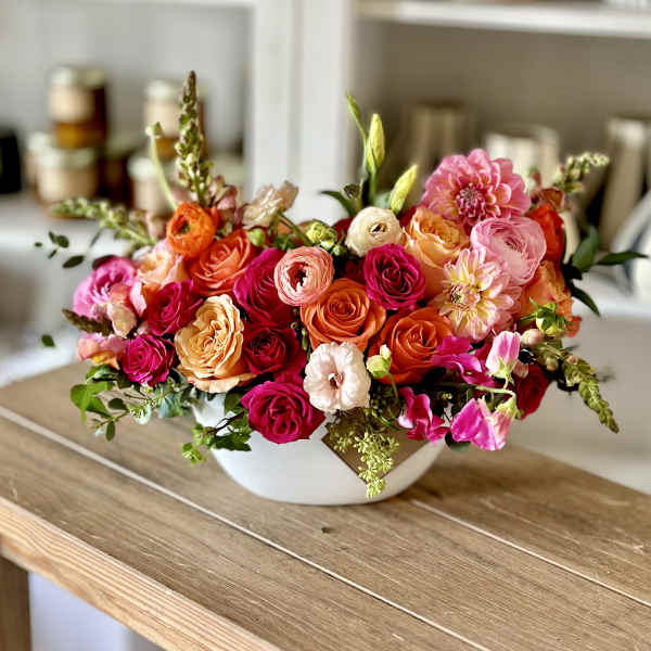 Mixed bouquet of pink, orange, and peach flowers in a white bowl vase