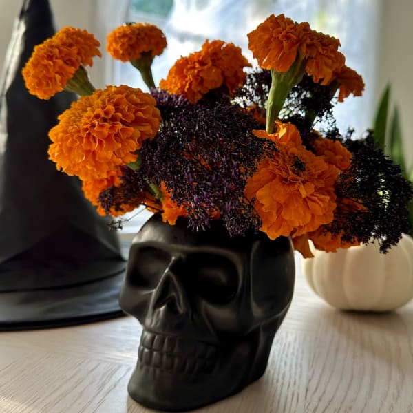 Orange marigolds arranged in a black skull vase with dark filler flowers