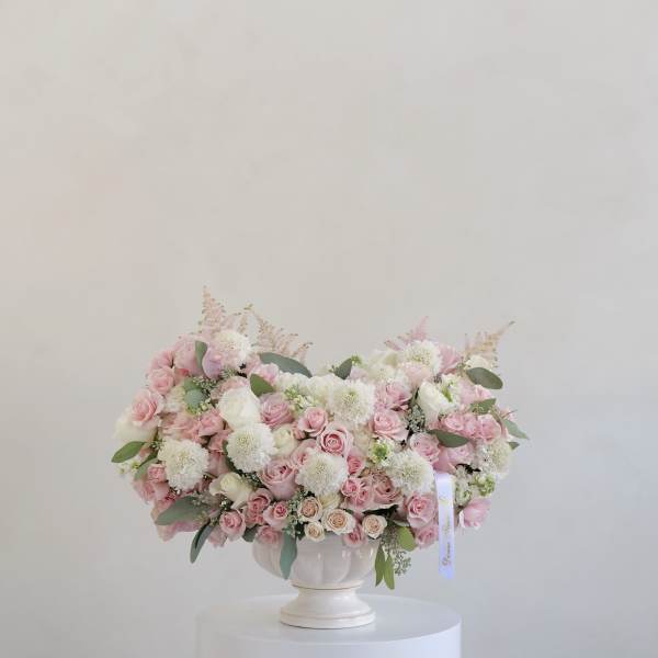 Pink and white rose arrangement in a white pedestal vase