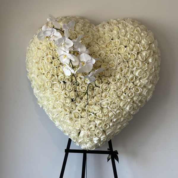 Heart-shaped arrangement of white roses with white orchids on a stand