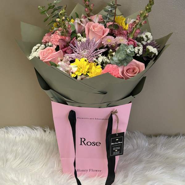 Mixed bouquet of pink roses, yellow blooms, and lavender flowers in a pink gift bag