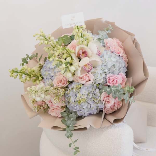 Pastel bouquet of pink roses, blue hydrangeas, and white orchids wrapped in beige paper