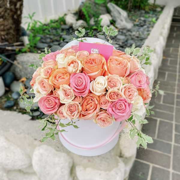 Round bouquet of pink, peach, and cream roses in a white hat box