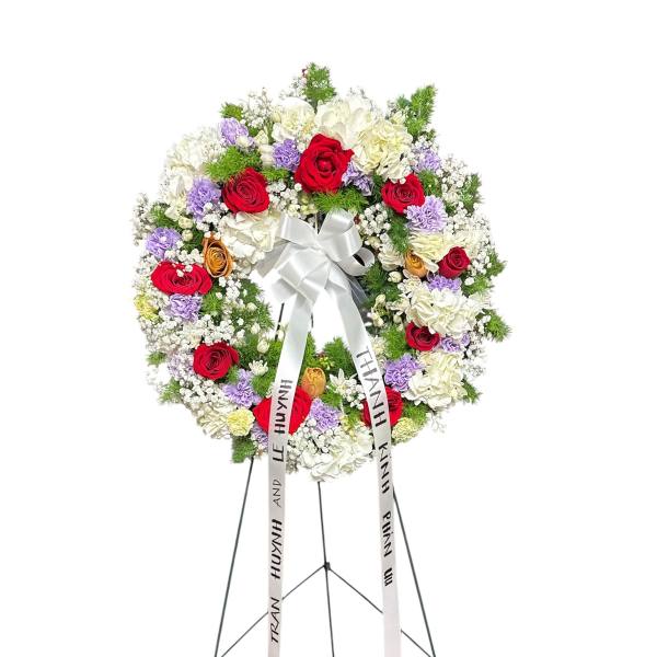 Circular funeral wreath of red, white, and lavender flowers on a stand