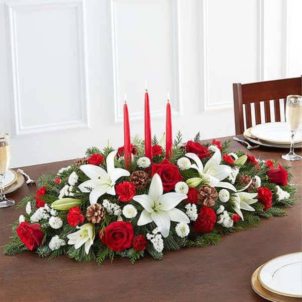 Holiday centerpiece with red candles, white lilies, and red roses on a table