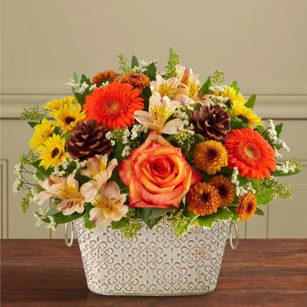 Mixed bouquet in a patterned white metal container with orange and yellow flowers