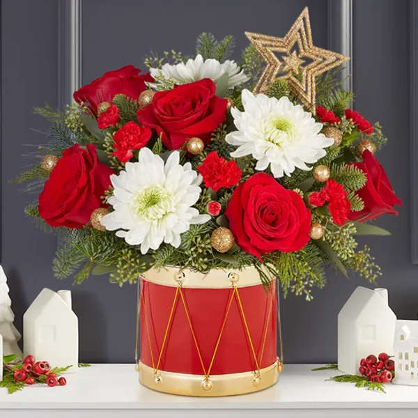 Red roses and white daisies arranged in a red drum container with a gold star topper.