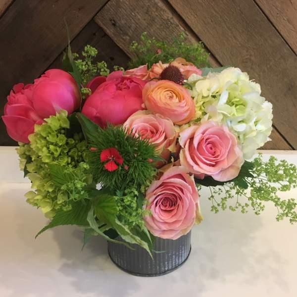 Pink and peach roses arranged with green and white hydrangeas in a metal container