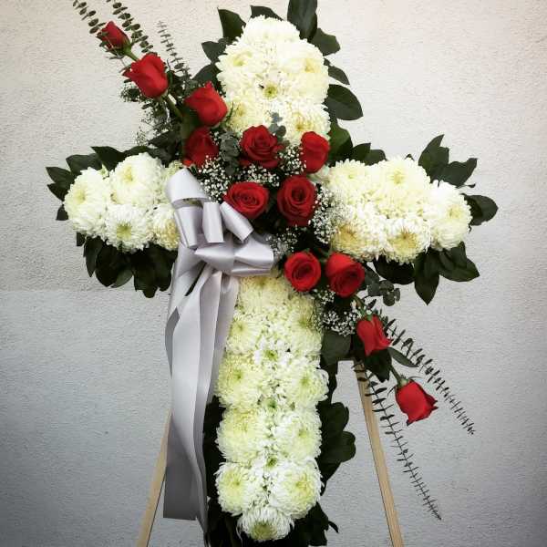 Cross-shaped floral tribute with white chrysanthemums and red roses, tied with a silver ribbon