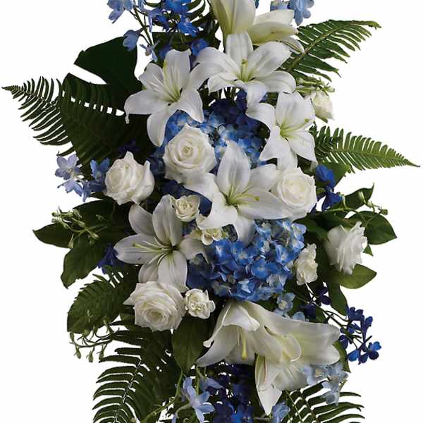 Standing floral spray with white lilies, white roses, and blue flowers on an easel