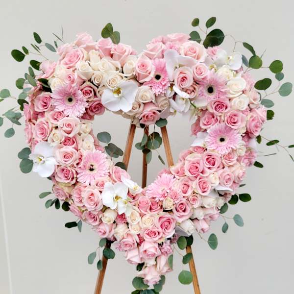 Heart-shaped floral arrangement of pink and white roses with orchids and daisies