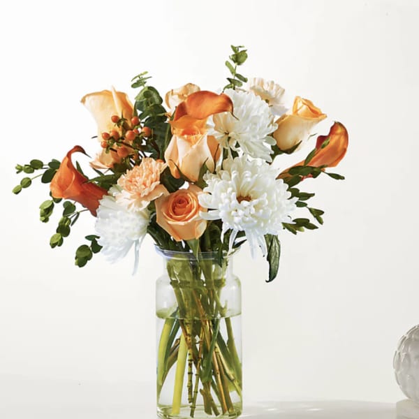 Bouquet of orange roses, white chrysanthemums, and orange calla lilies in a glass vase