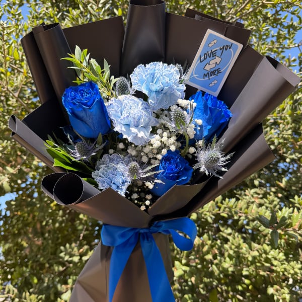 Blue roses and light blue carnations in dark wrap with a blue ribbon