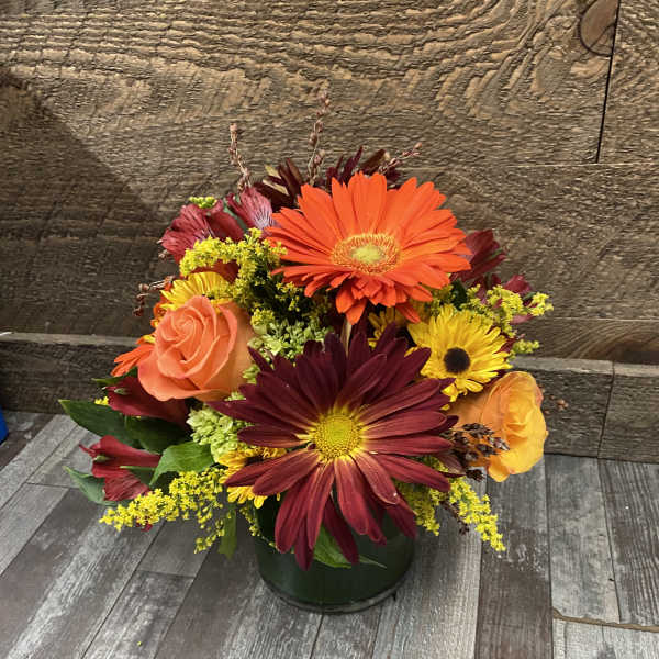 Mixed bouquet of orange, yellow, and burgundy flowers in a dark vase