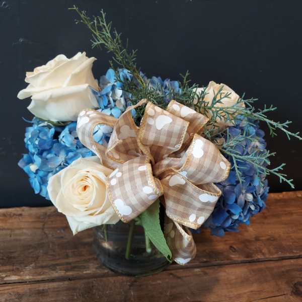 White roses and blue hydrangeas in a glass vase with a plaid ribbon