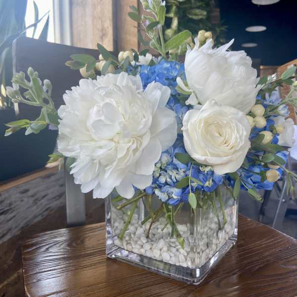 White and blue floral arrangement in a clear square vase