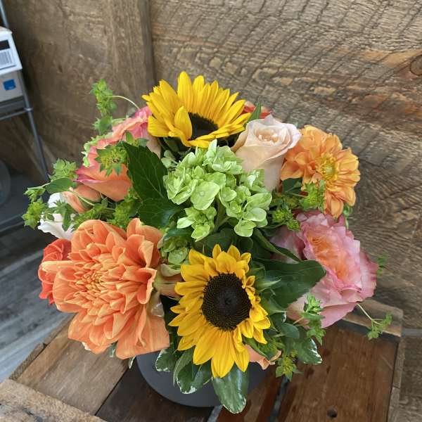 Bouquet of sunflowers, peach roses, and orange dahlias in a dark vase