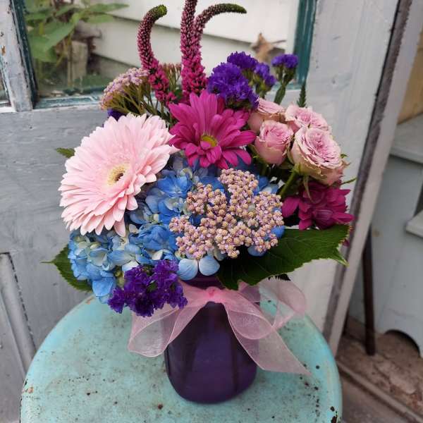 Colorful bouquet in a purple vase with a pink ribbon