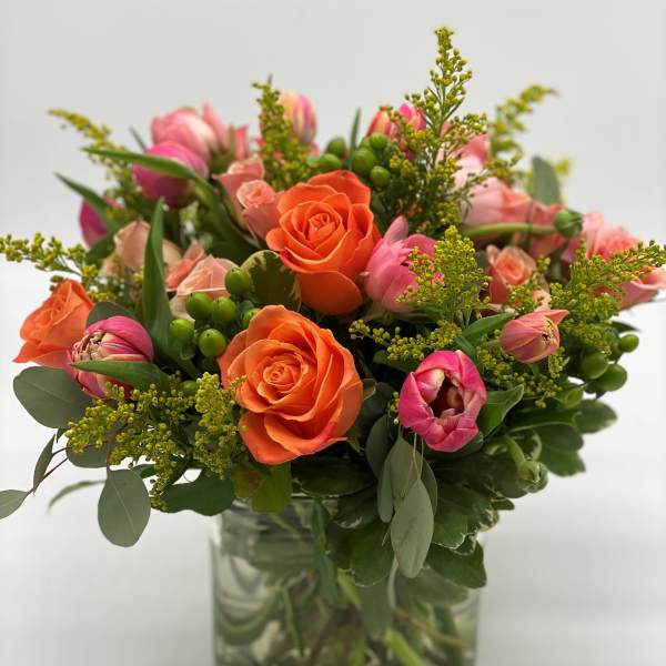 Orange roses and pink tulips in a clear glass vase