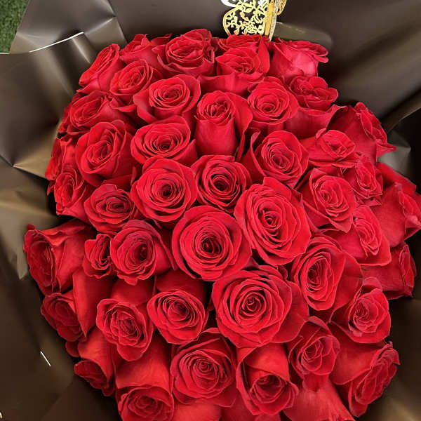 Bouquet of red roses wrapped in dark paper with a gold butterfly pick