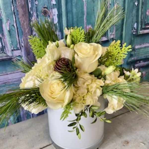 Cream floral arrangement in a white vase with long greenery accents